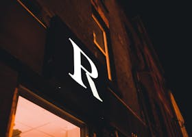 Close-up of an illuminated storefront sign with the letter "R" against a dark night sky.